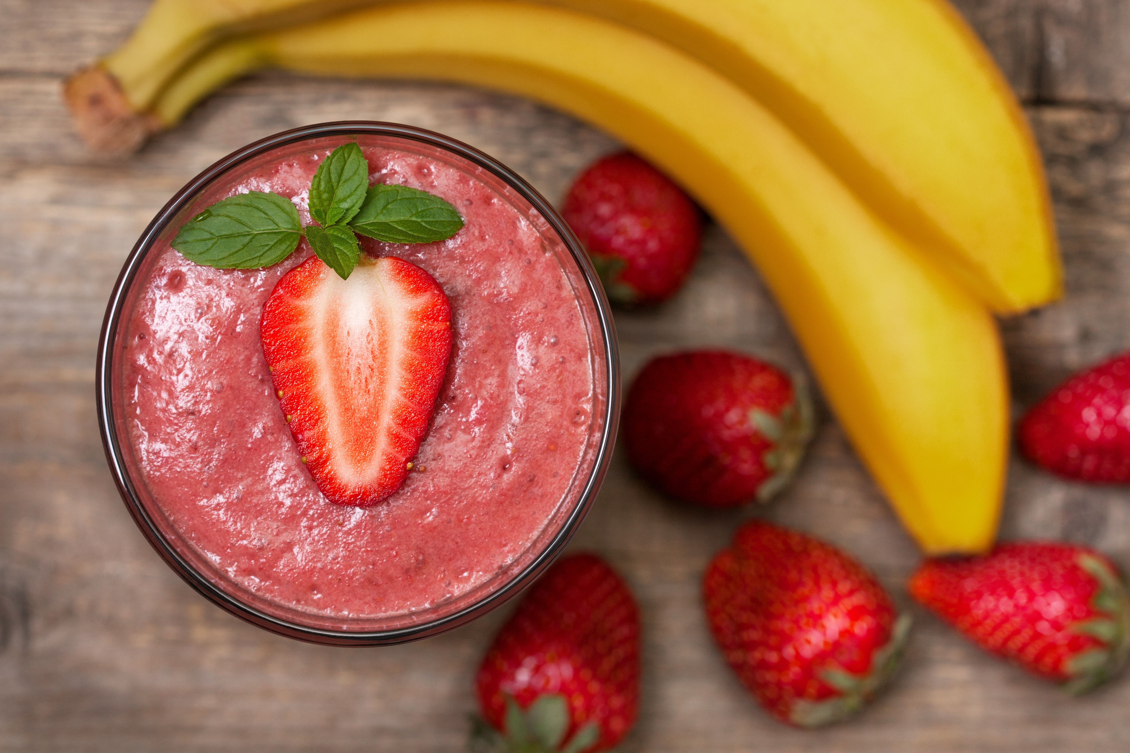 smoothie with banana and strawberry in the glass, fresh strawberries and bananas on the old wooden background