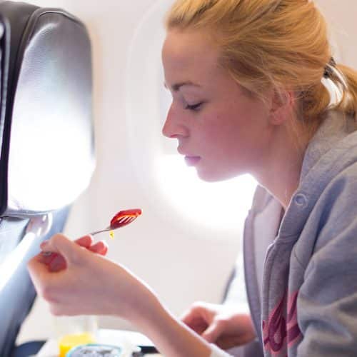 Woman eating meal on commercial airplane.