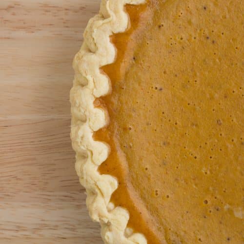 A very close view of a fresh pumpkin pie on a wood table top.