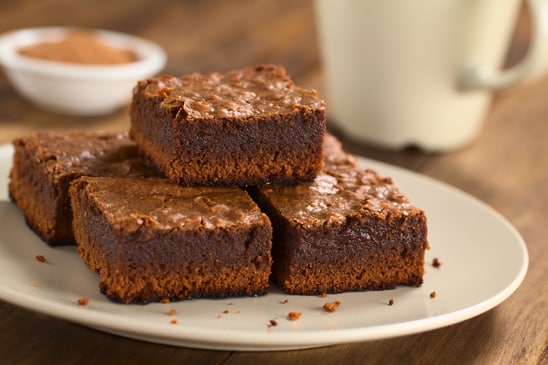 Freshly baked brownie pieces on a plate with cup in the back (Selective Focus, Focus on the left front part of the upper brownie)