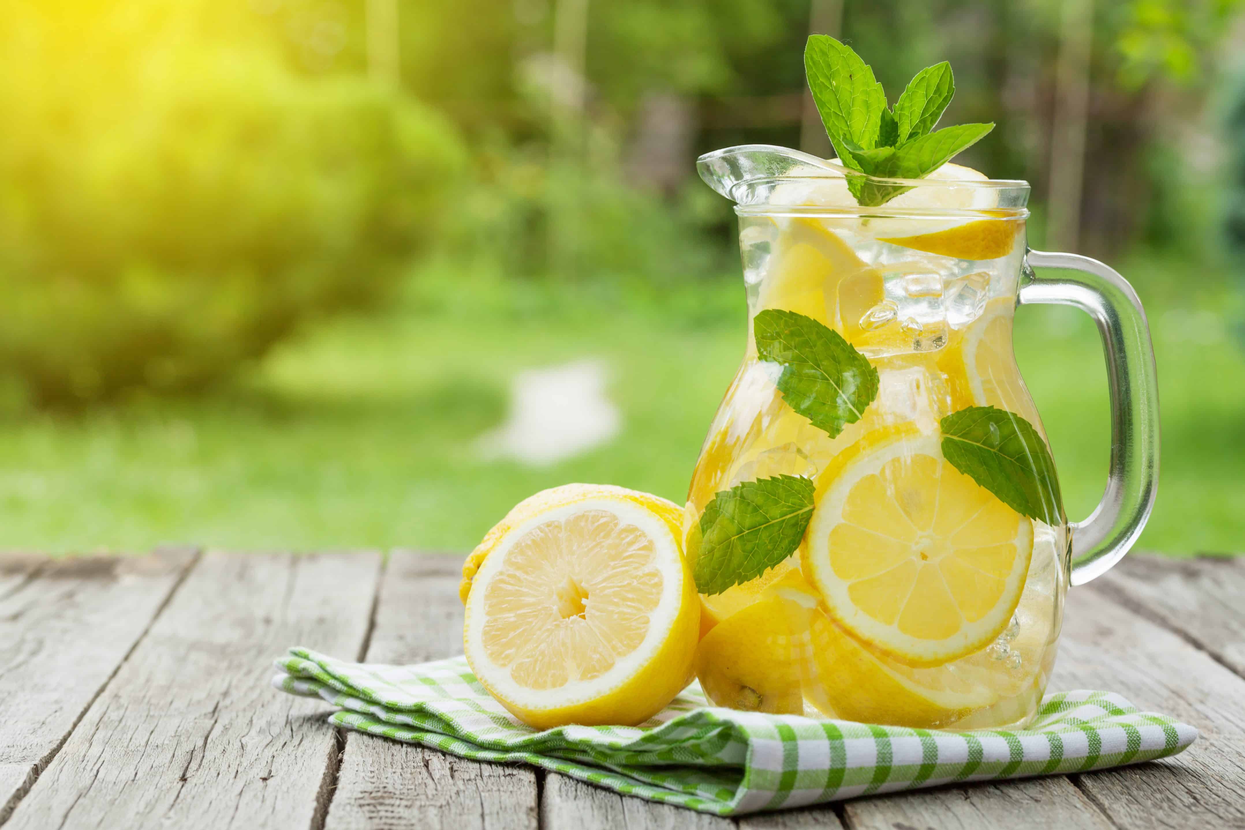 Lemonade pitcher with lemon, mint and ice on garden table. View with copy space