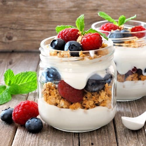 Blueberry and raspberry parfaits in mason jars, still life against a rustic wood background