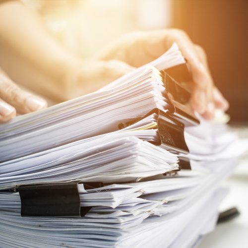 Businessman searching data in Stack of papers files on work desk in office, business report paper or piles of unfinished documents achives with clips on offices desk, Business concept